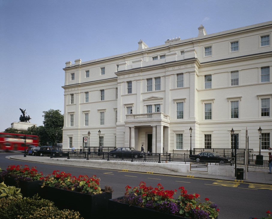 Whitewashed Georgian exterior of The Lanesborough hotel on Hyde Park Corner in London with classical architecture, columns, and red flowers in foreground.