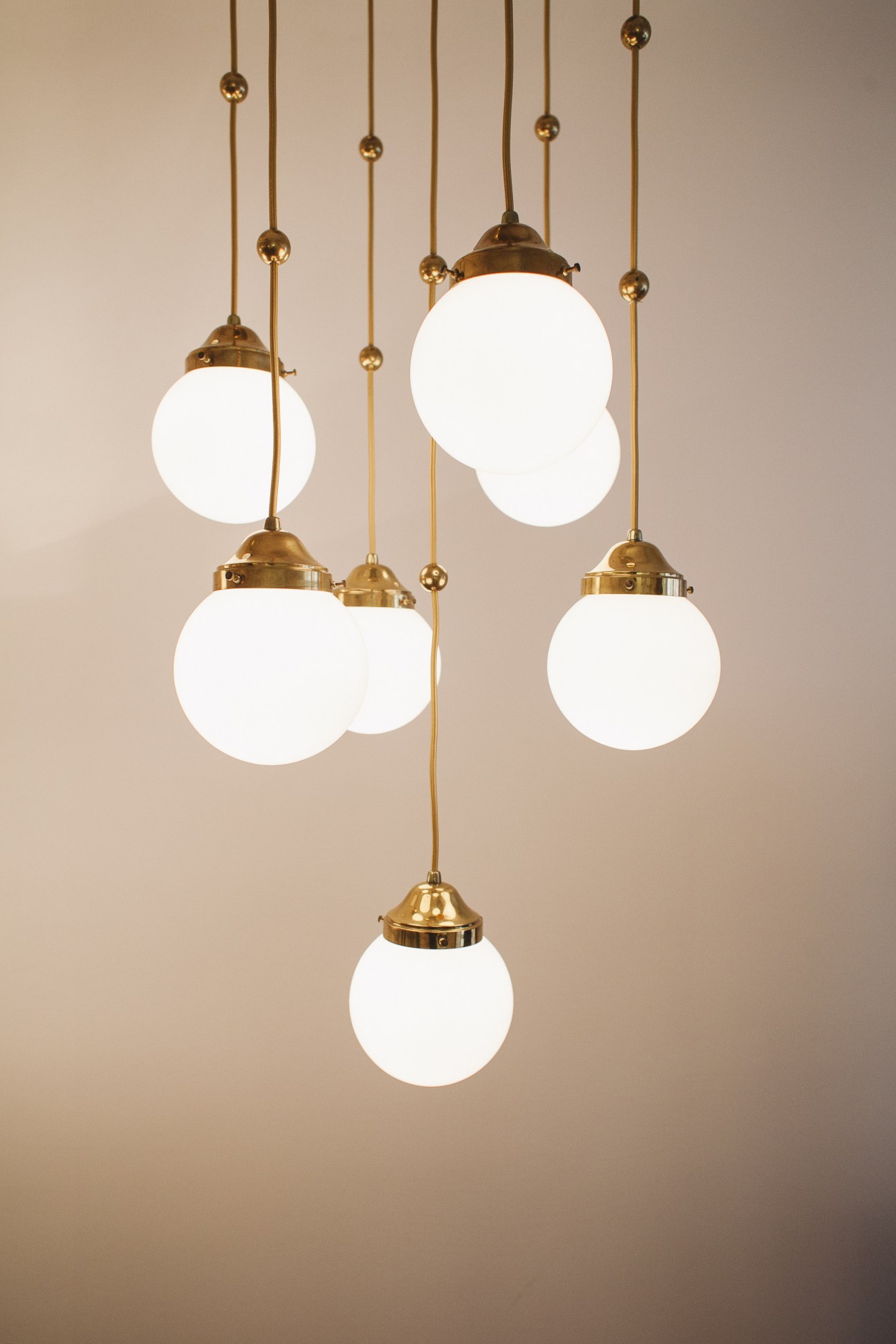Multiple brass pendant lights with white globe shades hanging at varying heights against a neutral background.