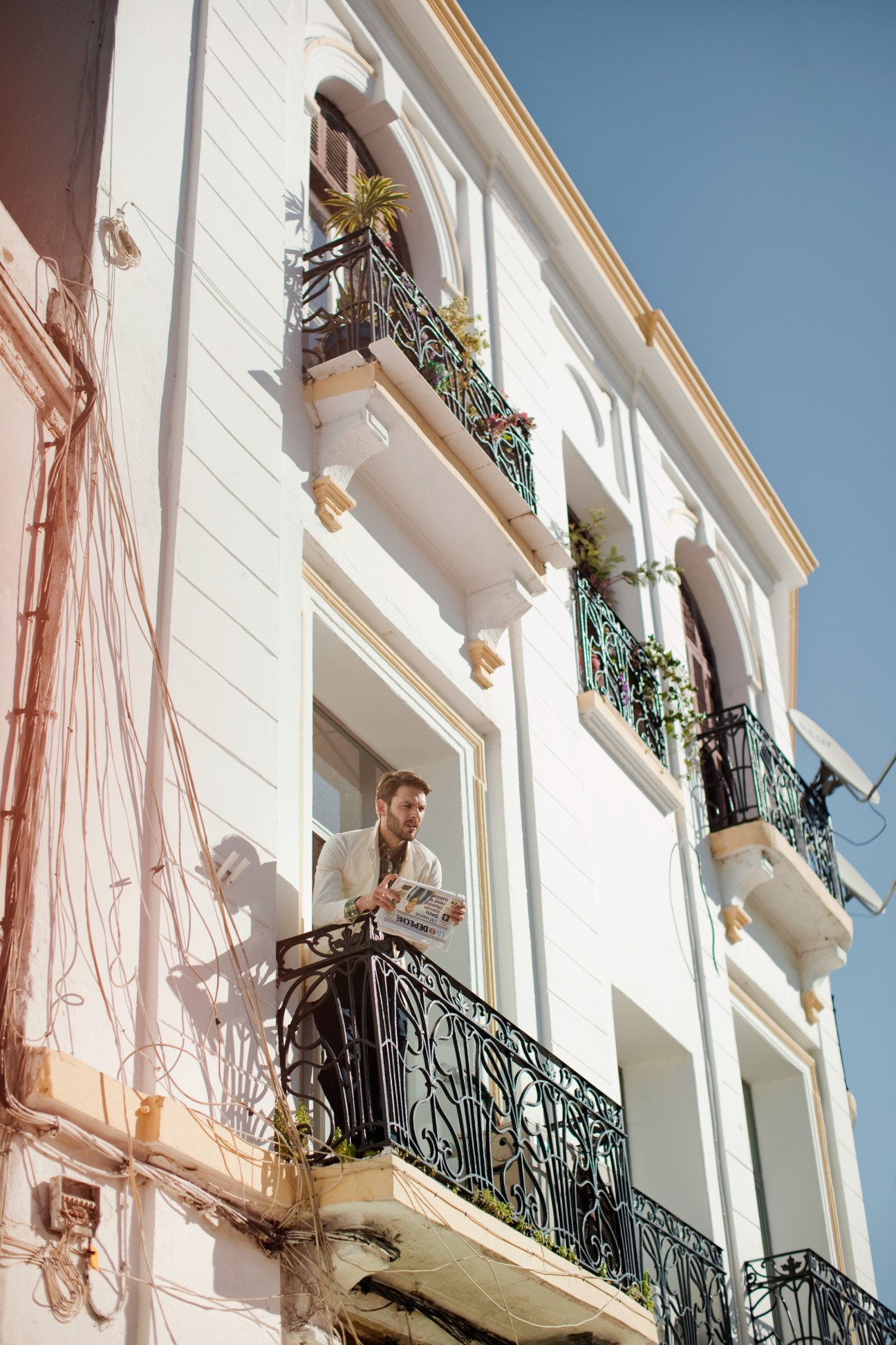 Man on a Tangier balcony wearing a Woolrich jacket and Engineered Garments shirt, holding a newspaper.