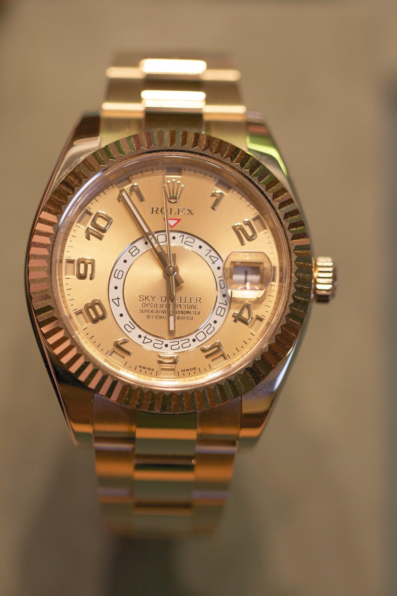 Rolex Sky-Dweller watch with gold dial and dual time zone functionality displayed on neutral background.