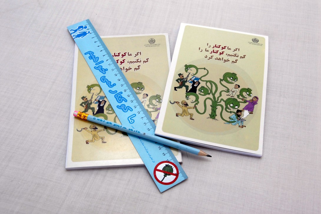 Afghan children's educational materials with anti-poppy messaging, including illustrated booklets and a blue ruler with warning symbols.