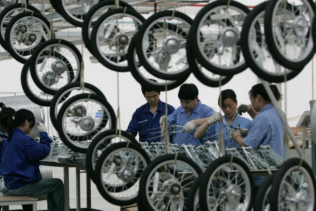 Workers in blue uniforms assembling bicycle wheels at Forever Bicycles manufacturing facility in China.