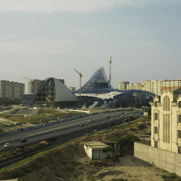Zaha Hadid's Heydar Aliyev Centre under construction in Baku, showing curved architectural forms and steel framework amid surrounding apartment buildings.