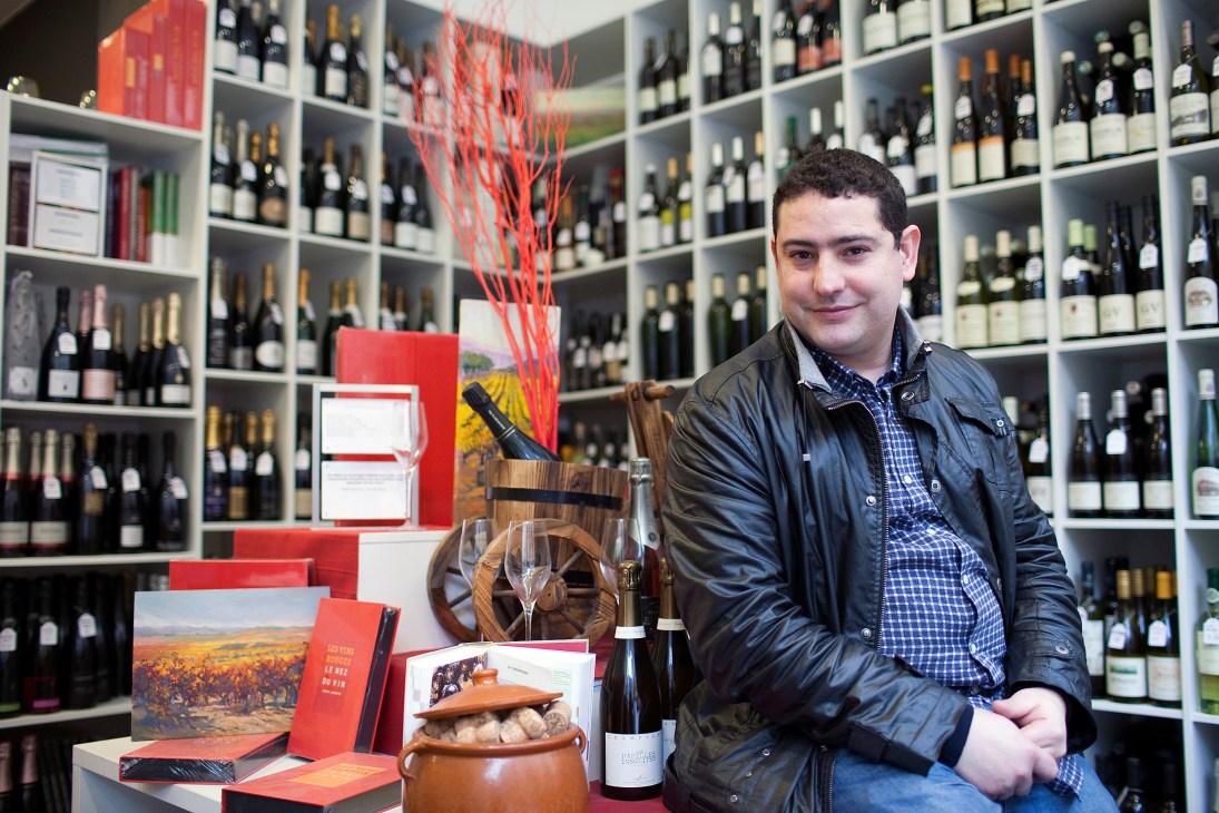 Dani Corman sits in his wine shop Essencia with shelves of bottles behind him.