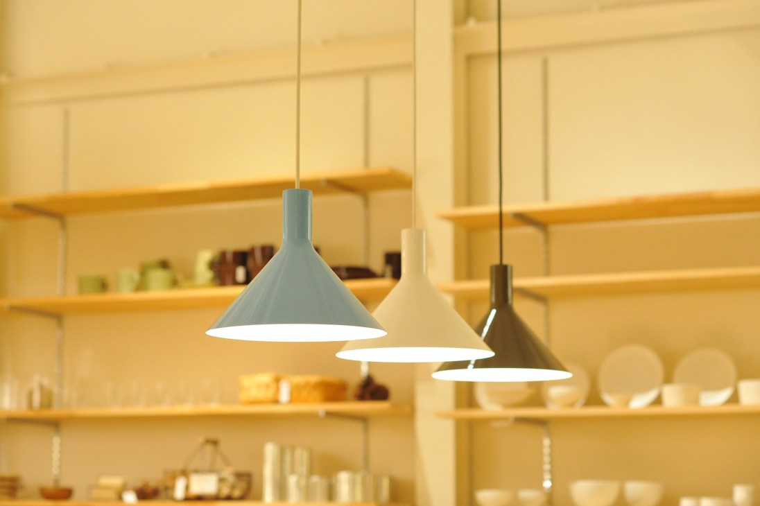 Three pendant lights with conical shades hanging in a warm-lit interior space with shelving.