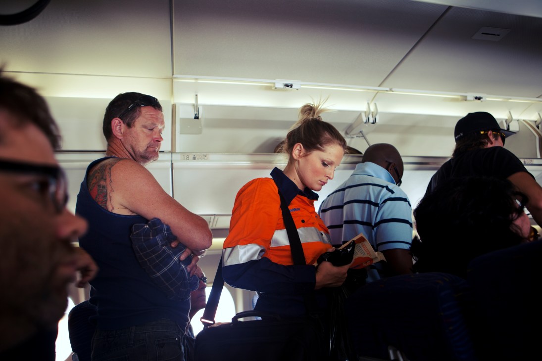 A female flight attendant serves a passenger on a crowded aircraft cabin during a FIFO mining worker flight.