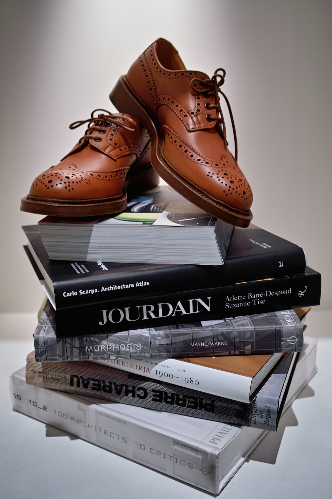 Tan brogue oxford shoes displayed atop a stack of design and architecture books.