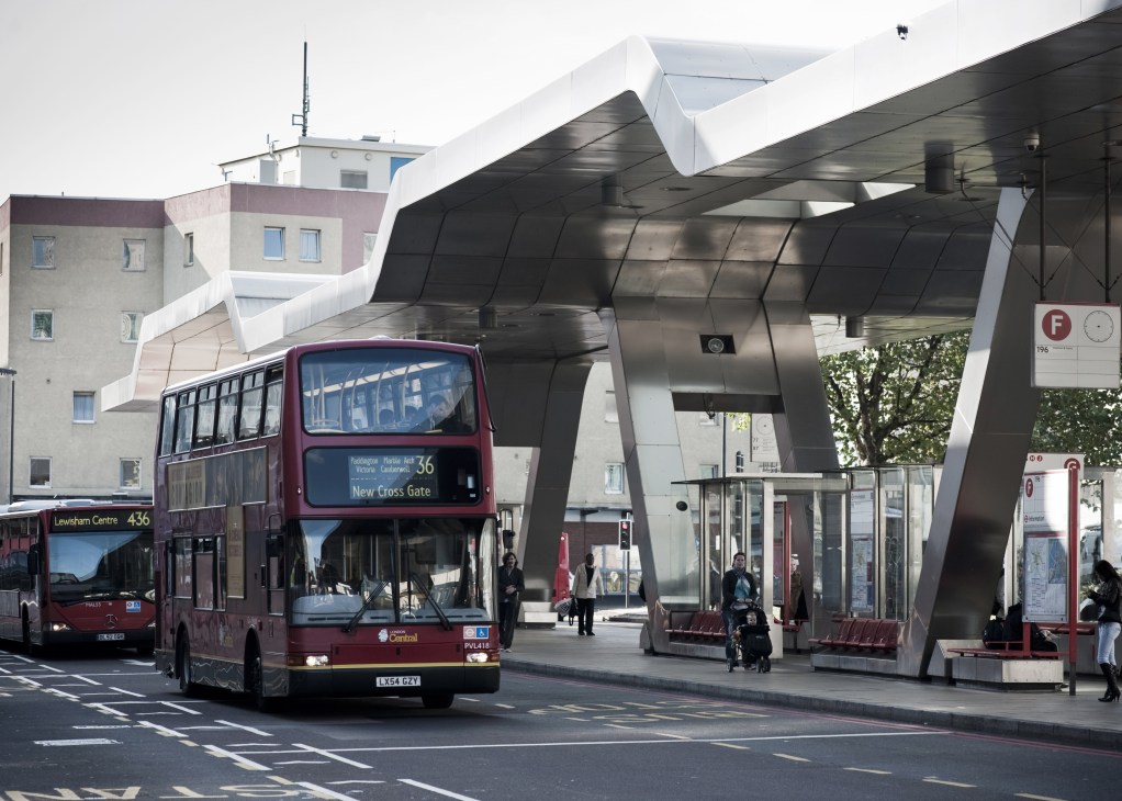Modern white cantilevered canopy structure at Vauxhall Tube station with red double-decker bus passing beneath.