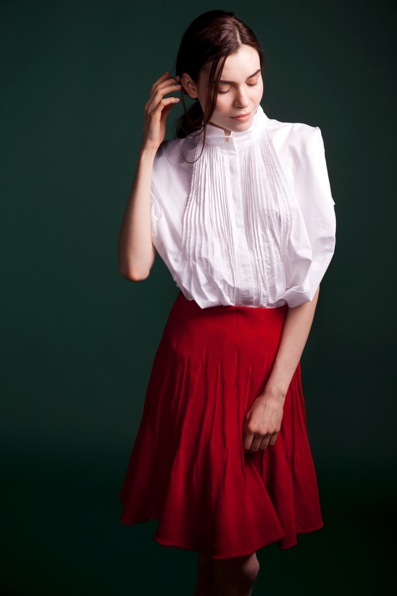 Woman wearing a white pleated blouse and red skirt against a green background.