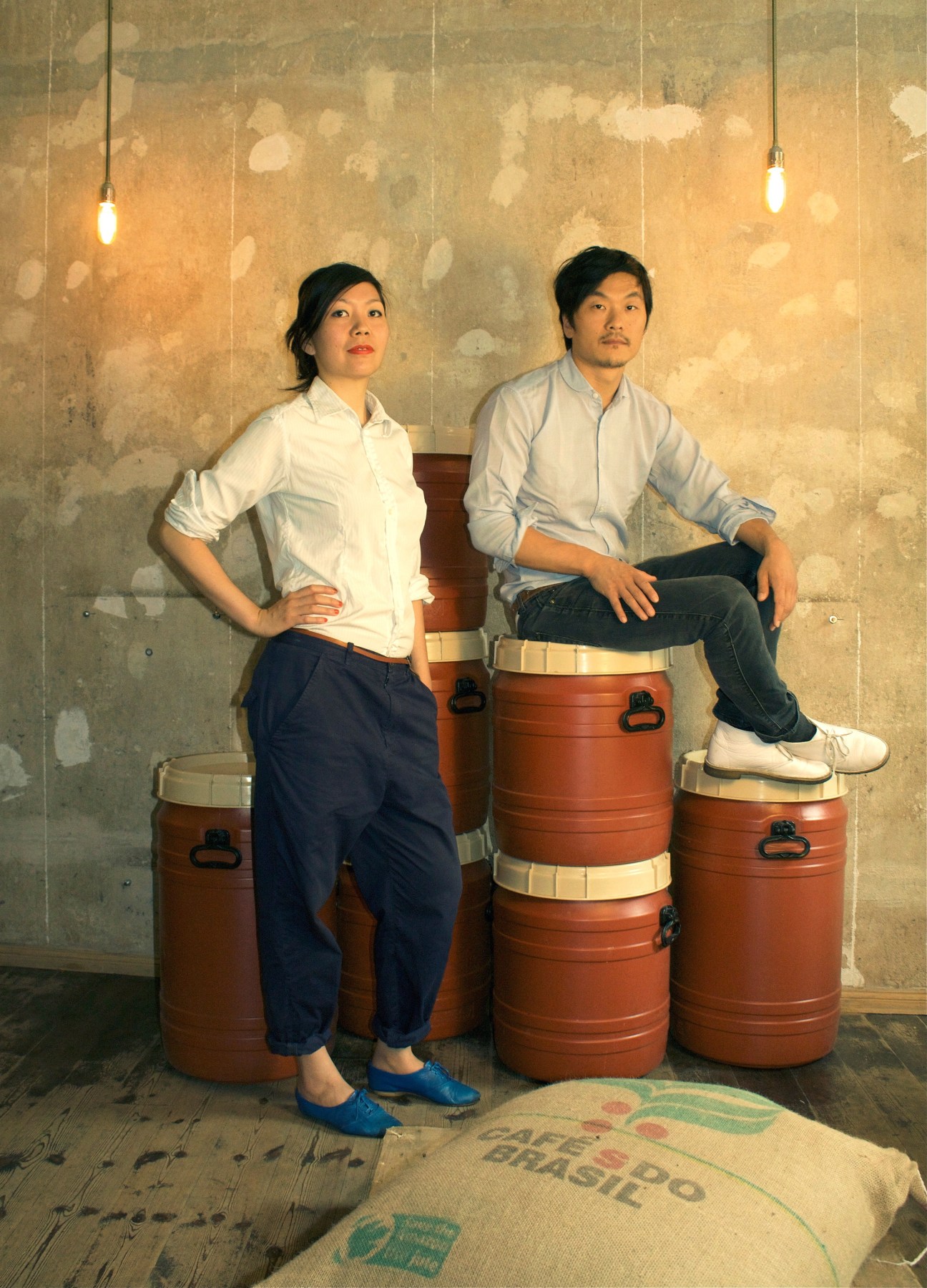 Yumi Choi and Kiduk Reus, founders of Bonanza Coffee Heroes, sitting on coffee drums in their Berlin café.
