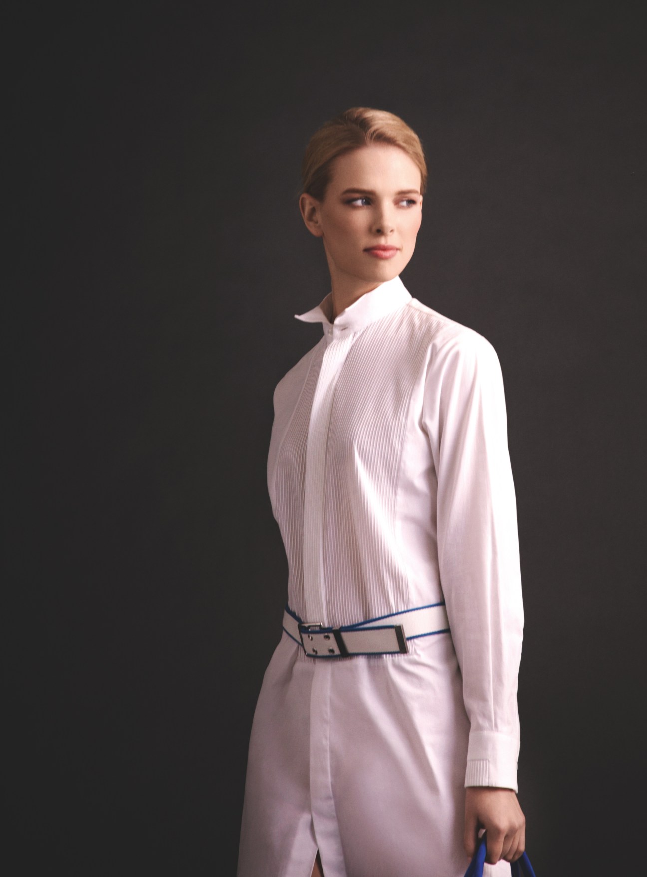 Model wearing pale pink dress by 1205 with Hermès belt and Roger Vivier bag against dark background.