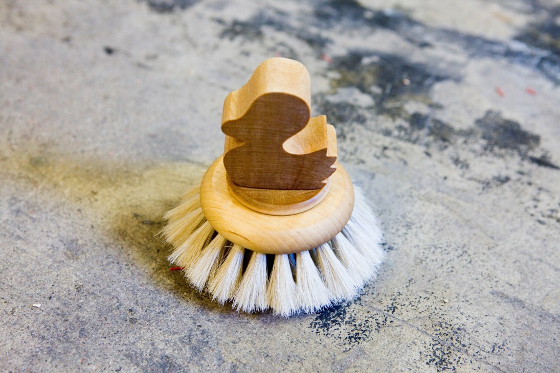 Iris Hantverk Bath Duck brush with wooden handle and white bristles on a textured surface.