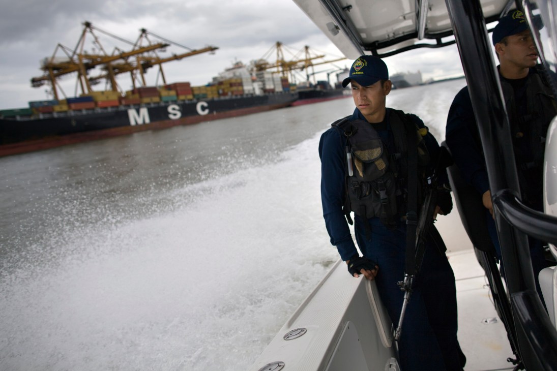 Armed Colombian naval personnel on patrol boat searching for drug traffickers near cargo ship at Buenaventura port.