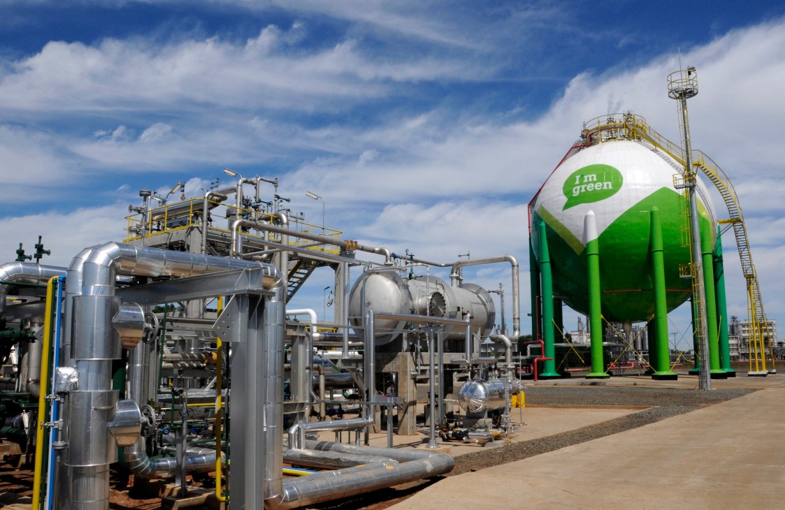 Industrial petrochemical facility with green storage tank labeled 'i'm green' and metal processing equipment under blue sky.