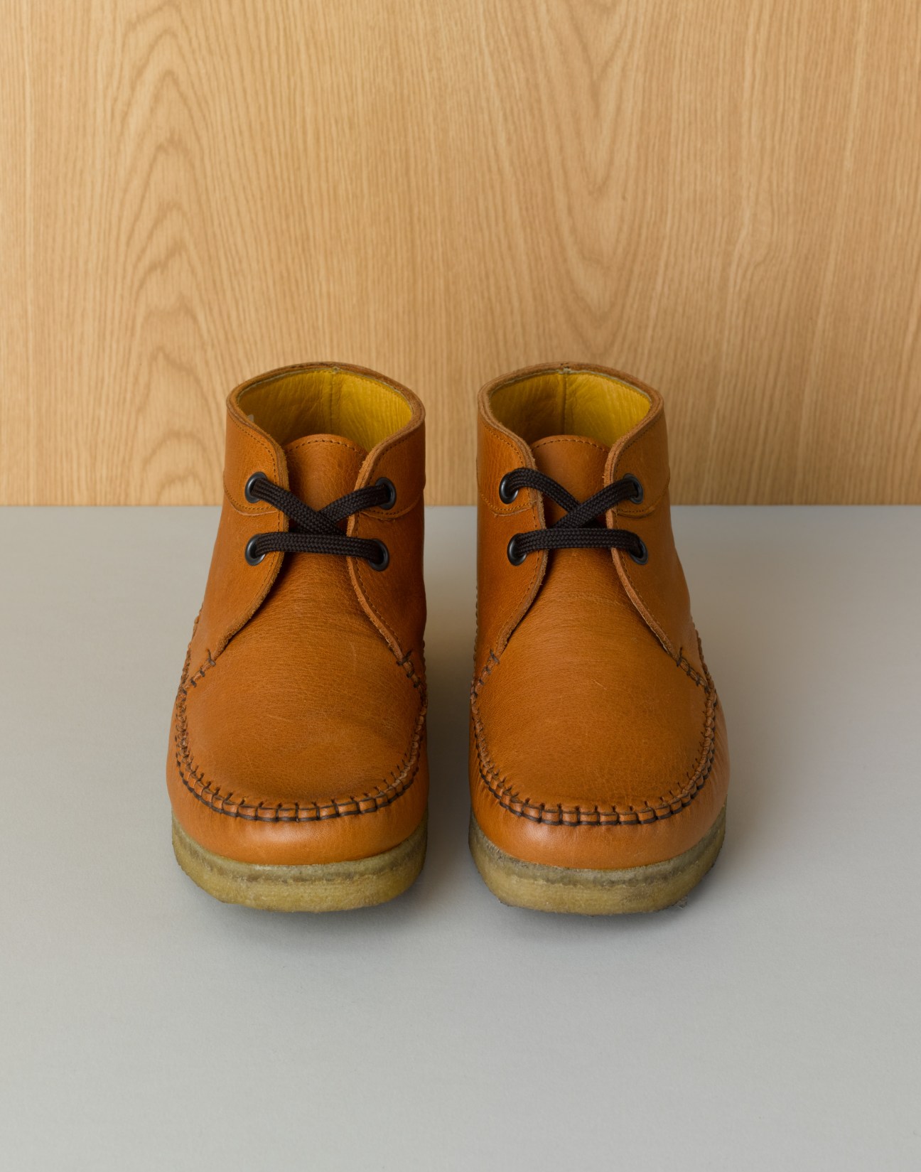 Pair of tan leather lace-up boots with crepe soles and yellow lining, displayed on white surface.