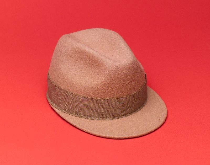 Beige wool cap with grosgrain ribbon band on coral red background.