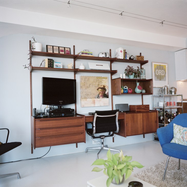 A modern apartment interior with mid-century furniture, including a wooden wall system with shelving, TV, and desk area in the Moddrell's Marina City unit.
