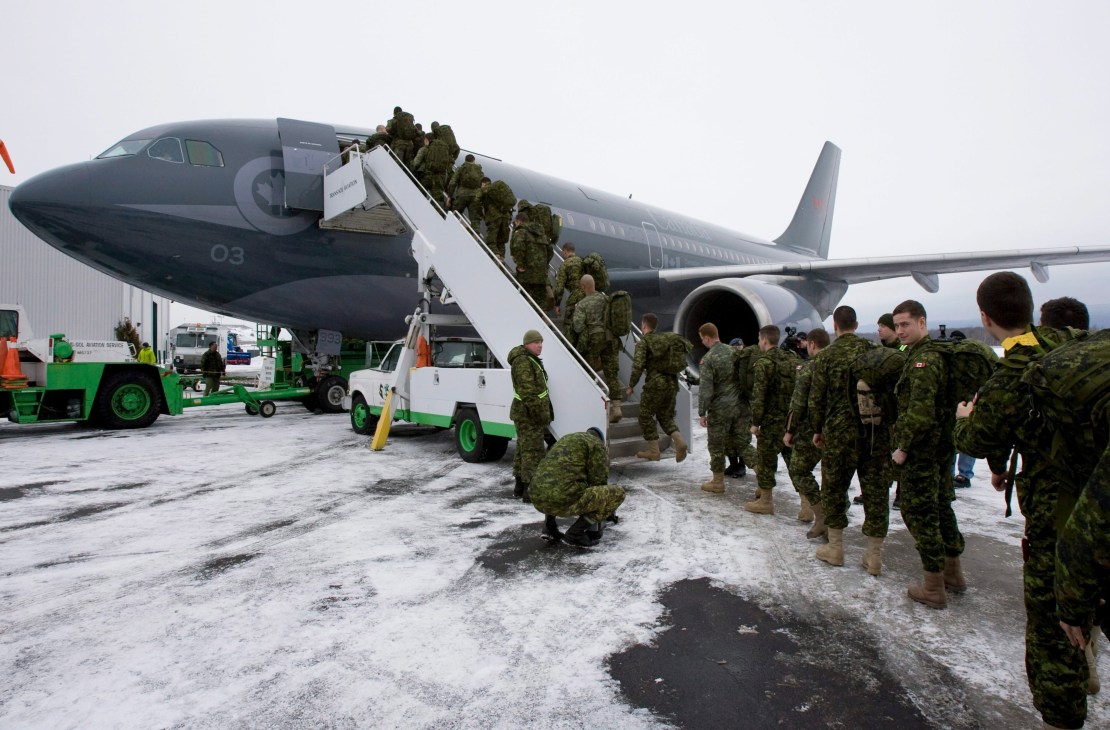 Canadian armed forces in camouflage uniforms boarding a large military transport aircraft at an airport.
