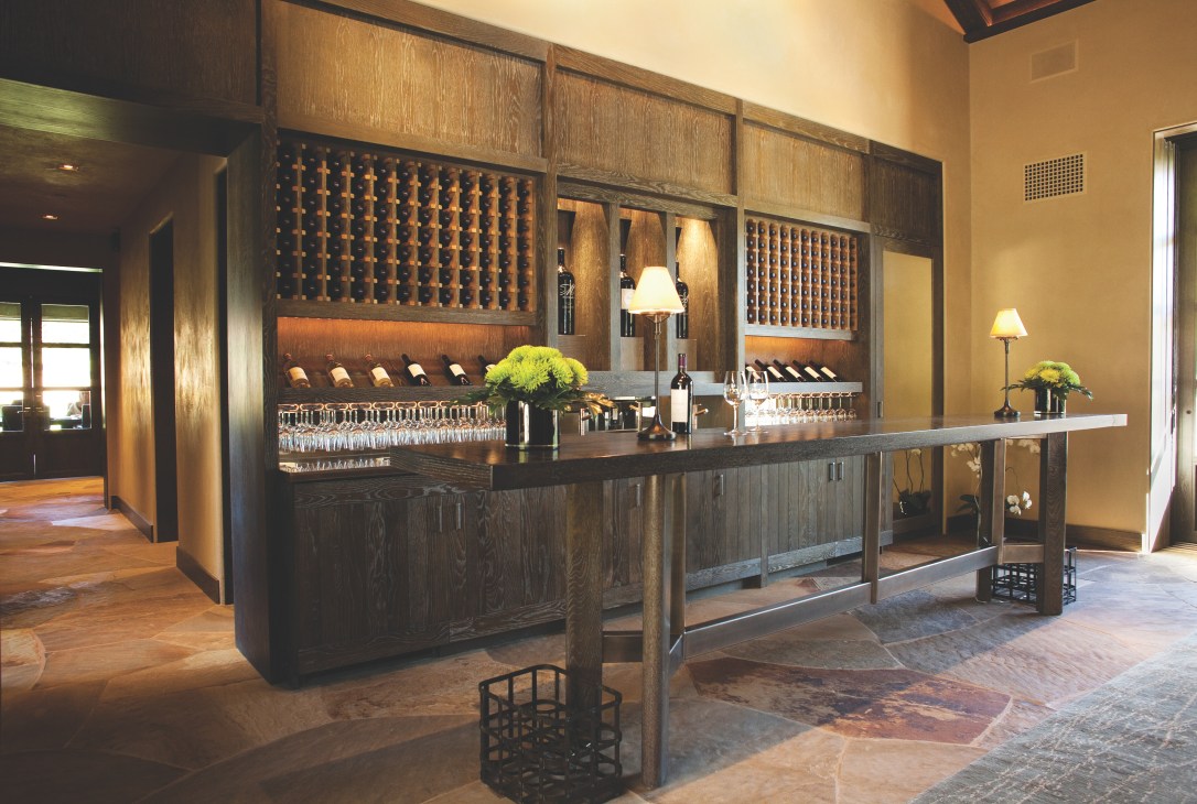 Modern wine tasting room with dark wood bar, wine storage displays, and contemporary lighting designed by architect Howard Backen.