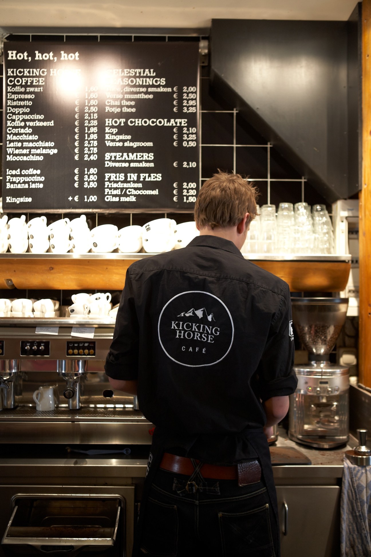 A barista in a black Kicking Horse Cafe jacket stands at an espresso machine behind the counter.
