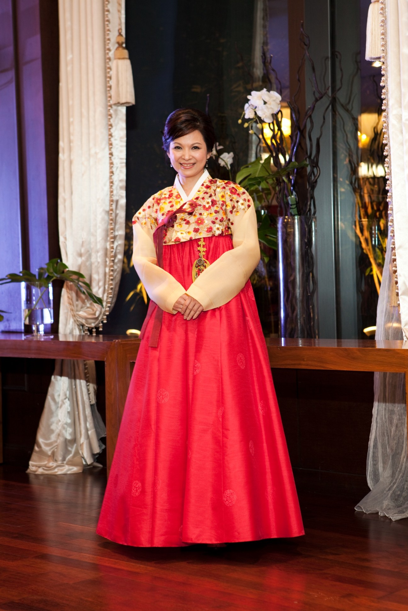 Taiwanese actress Yang Kuei-mei wearing a red traditional Korean hanbok dress with floral upper garment, standing in an elegant venue with white flowers and draped fabrics.