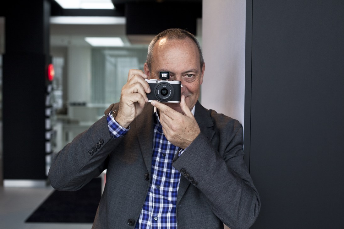 Man in business attire holding a Leica camera up to his face in an office setting.