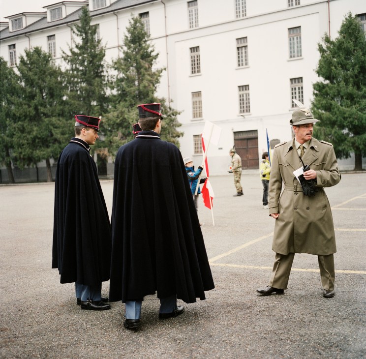 Italian police officers in ceremonial dress with capes stand in a barracks courtyard near a Polish flag.
