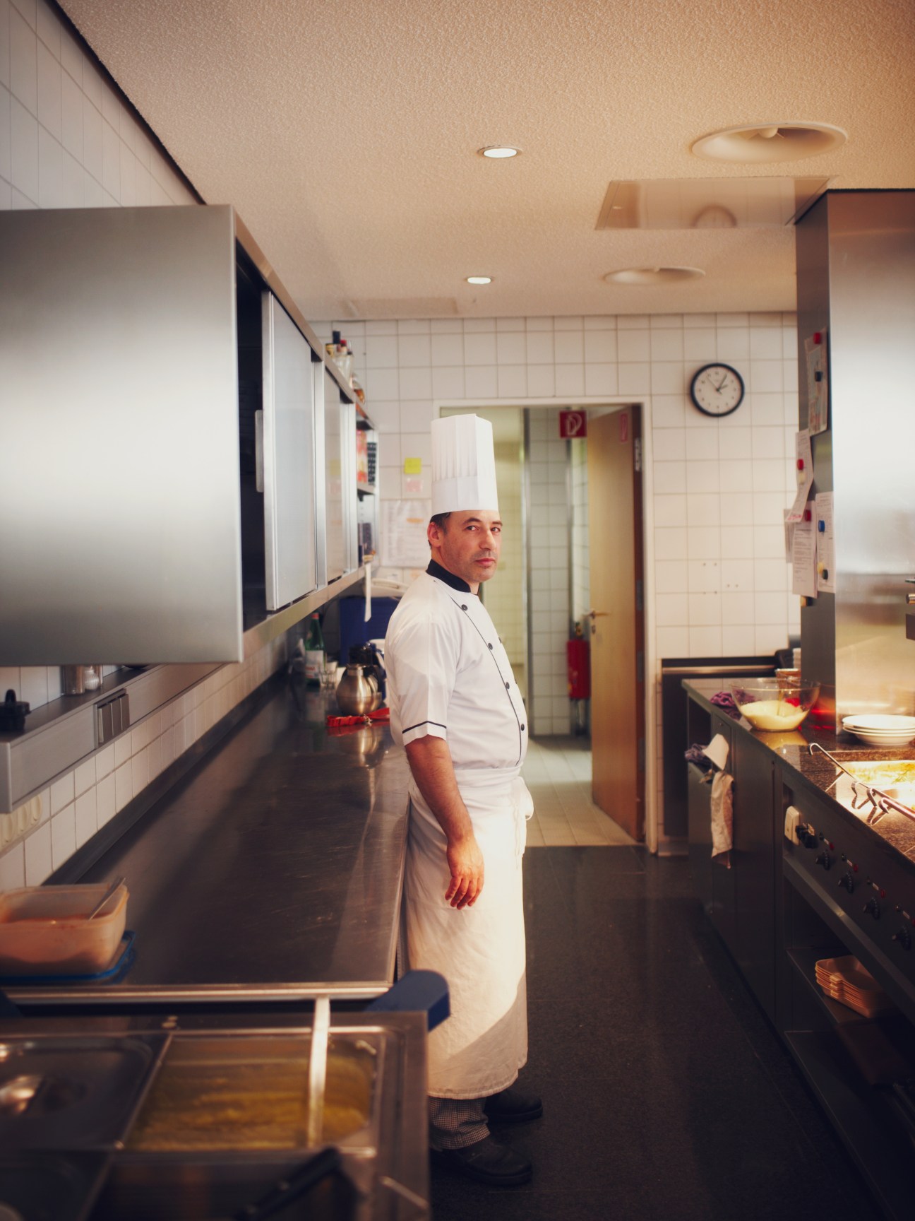 Italian chef Bruno Mazza in white chef's uniform and hat standing in a kitchen at the Goethe-Institut Munich headquarters.