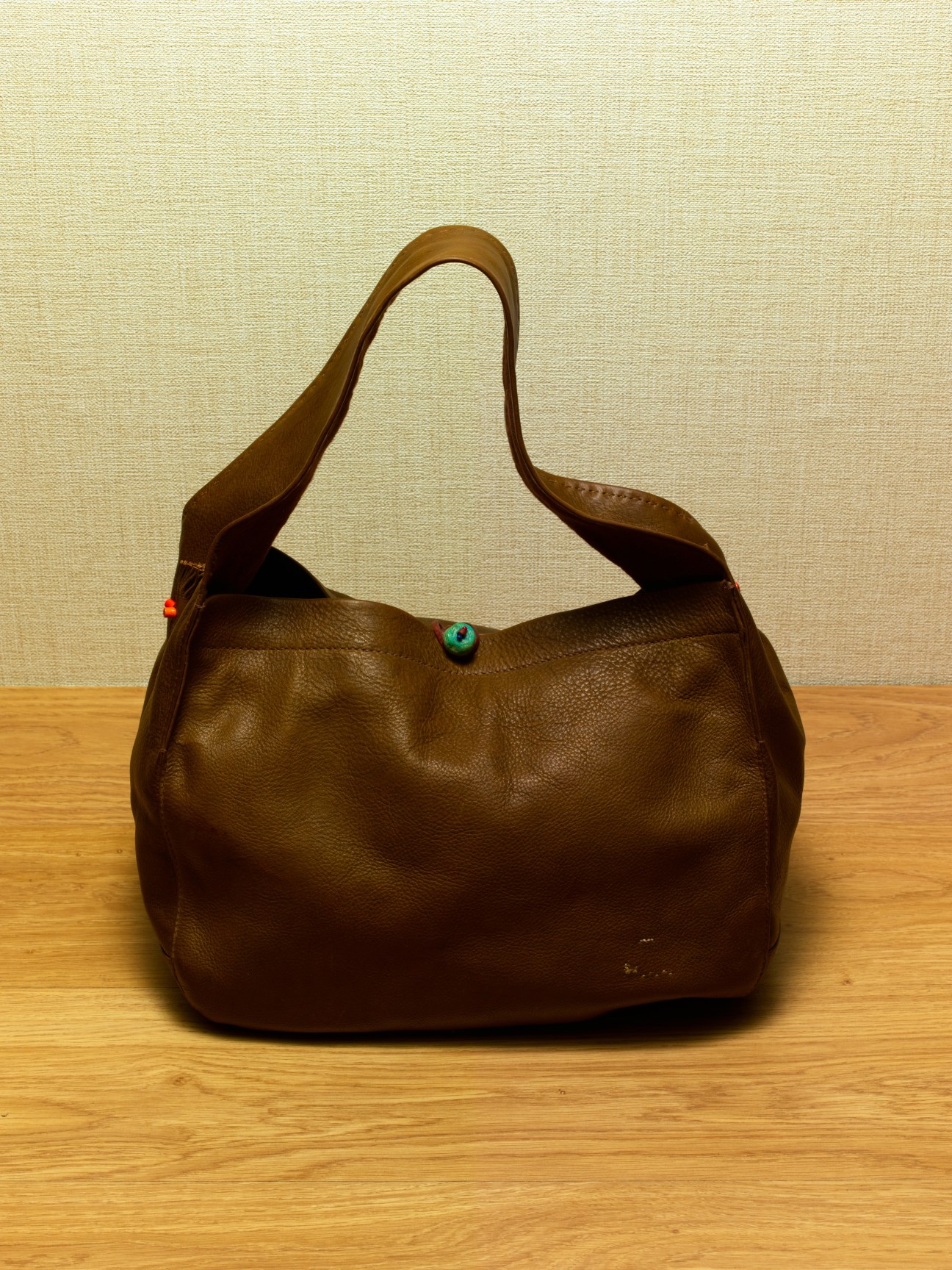 Brown leather shoulder bag with decorative button closure displayed on wooden surface.