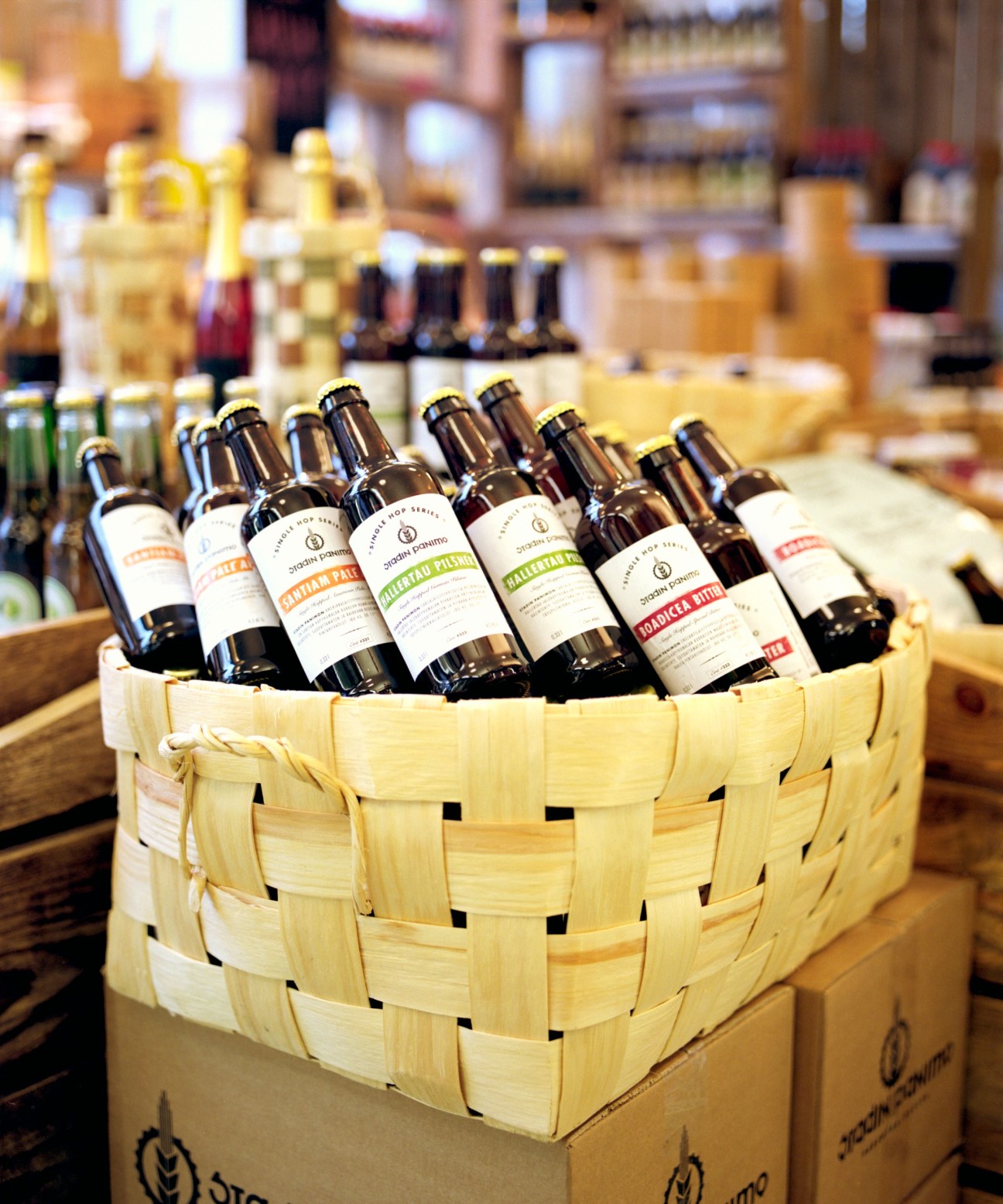 Craft beer bottles with white labels displayed in a woven wooden basket at Eat & Joy Farmers Market in Helsinki.