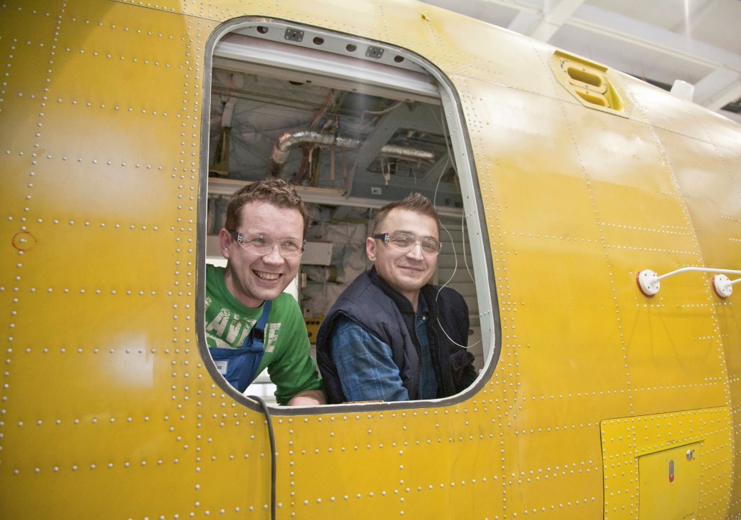 Two men look out from a window in the yellow fuselage of a helicopter at PZL Mielec.