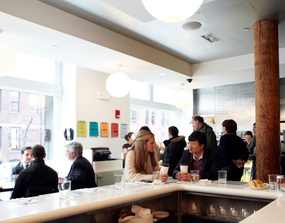 Diners seated at counter and tables inside Sportello restaurant with bright lighting and wooden support column