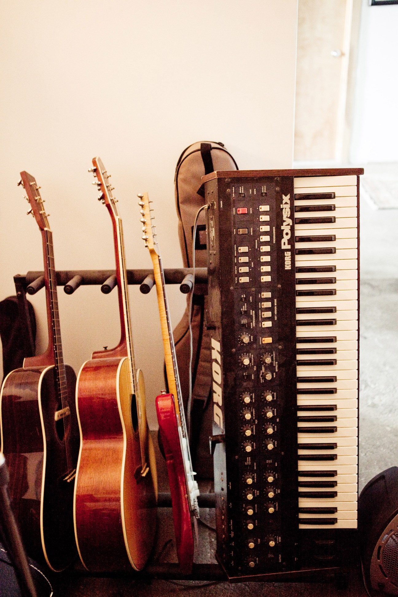 Guitars and a synthesizer keyboard arranged in Matthew Dear's studio against a cream wall.