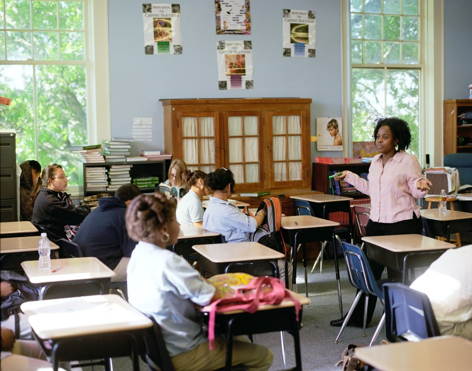 French teacher Diana Pierre-Louis instructing students in a bright classroom with large windows and educational posters.