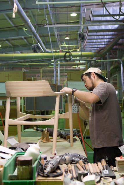 A craftsman sands a wooden chair frame in a factory workshop.
