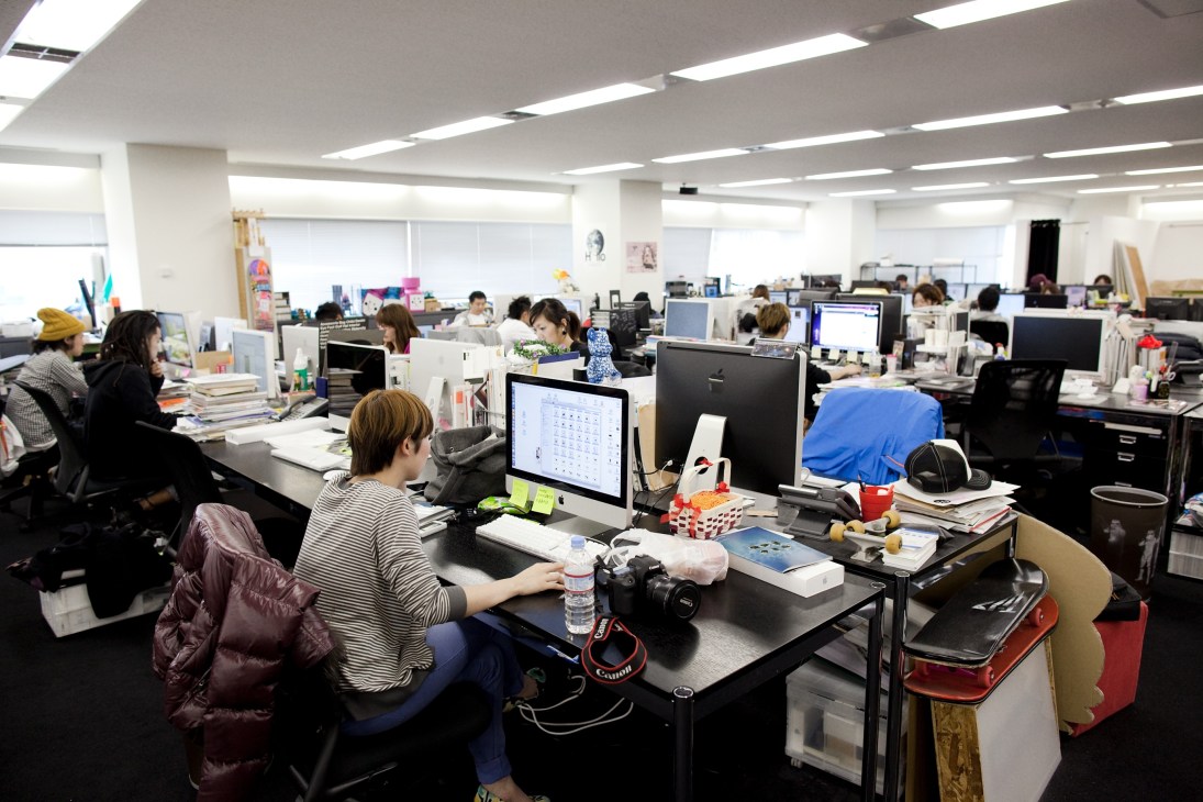 Open-plan office with employees working at computer desks in a bright, modern workspace.