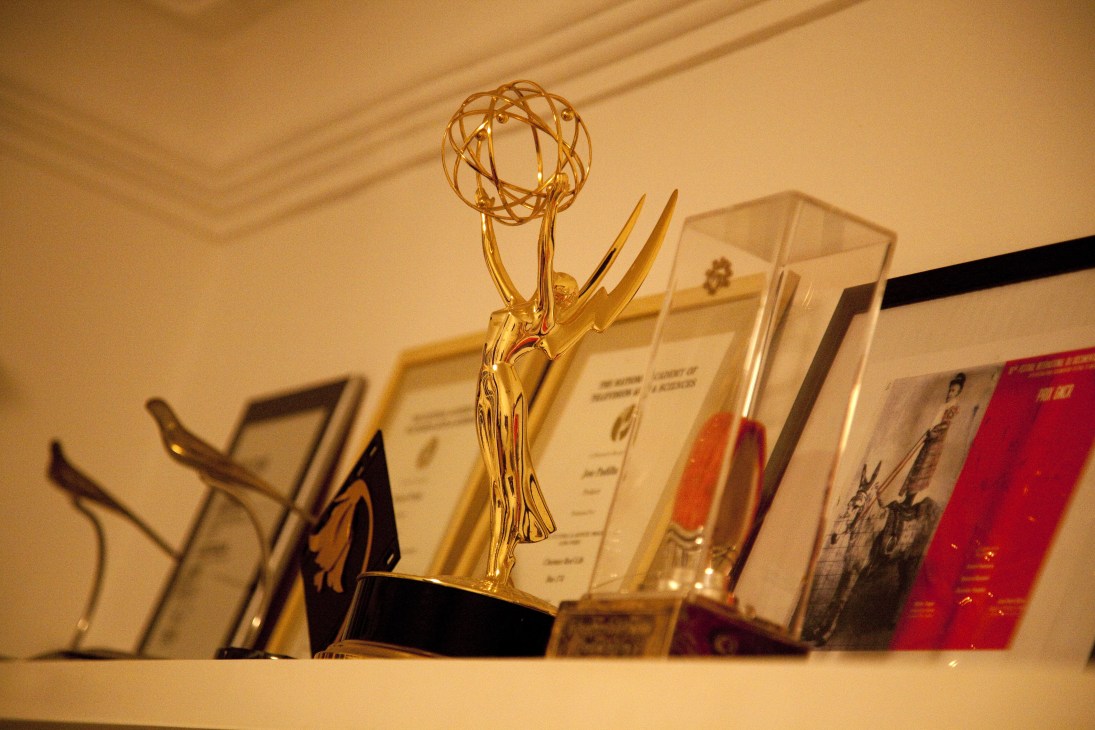 An Emmy Award displayed prominently among other awards and certificates on a shelf.