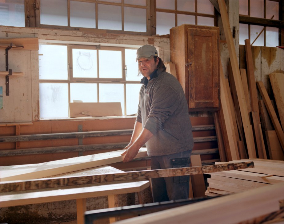 Carpenter in cap stands at workbench with wood planks in Horgenglarus factory mill.