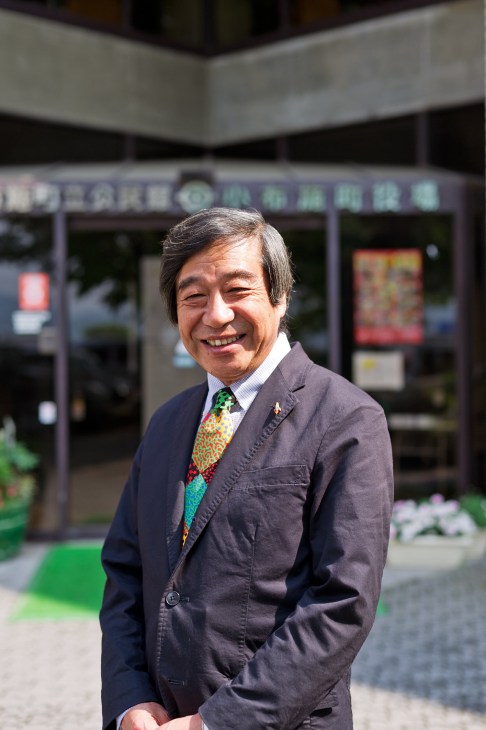 Ryozo Ichimura, Mayor of Obuse, smiling in front of a storefront in Japan.