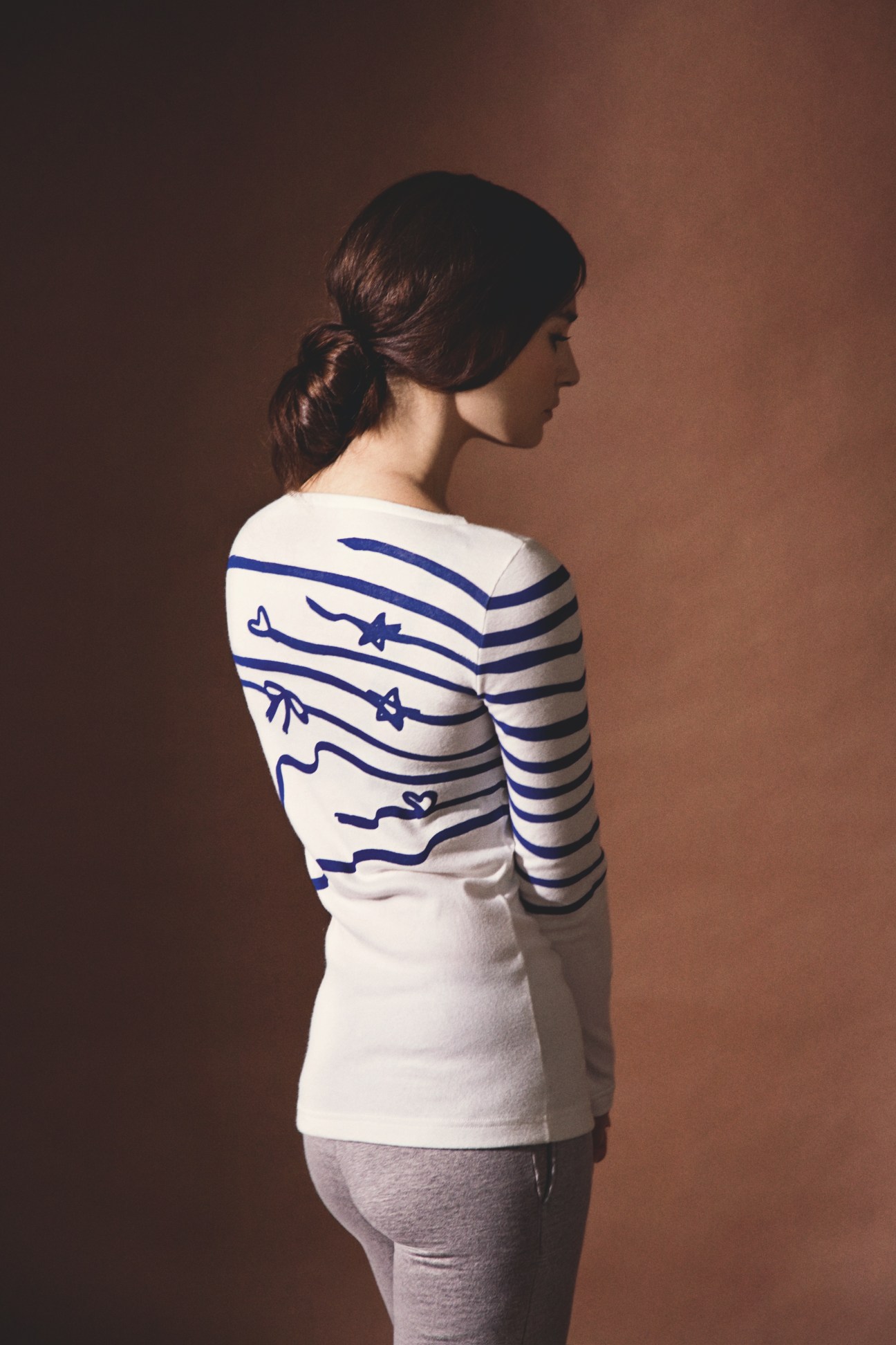 Woman wearing white and navy striped long-sleeve top with sailboat design from Tsumori Chisato x Petit Bateau collection.