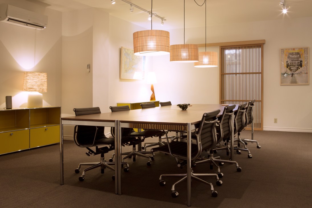 Modern meeting room with long table, black chairs, pendant lighting, and yellow storage cabinets.