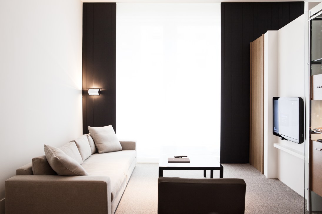 Modern hotel guest room with neutral furniture, dark wood accents, and wall-mounted lighting at Andaz Fifth Avenue.