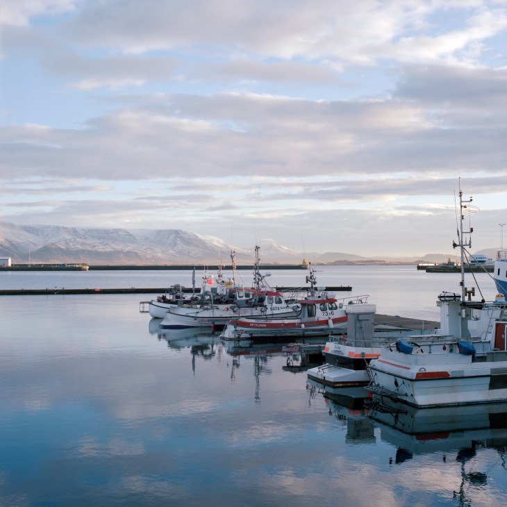 Fishing boats moored in calm water with snow-capped mountains in the background.