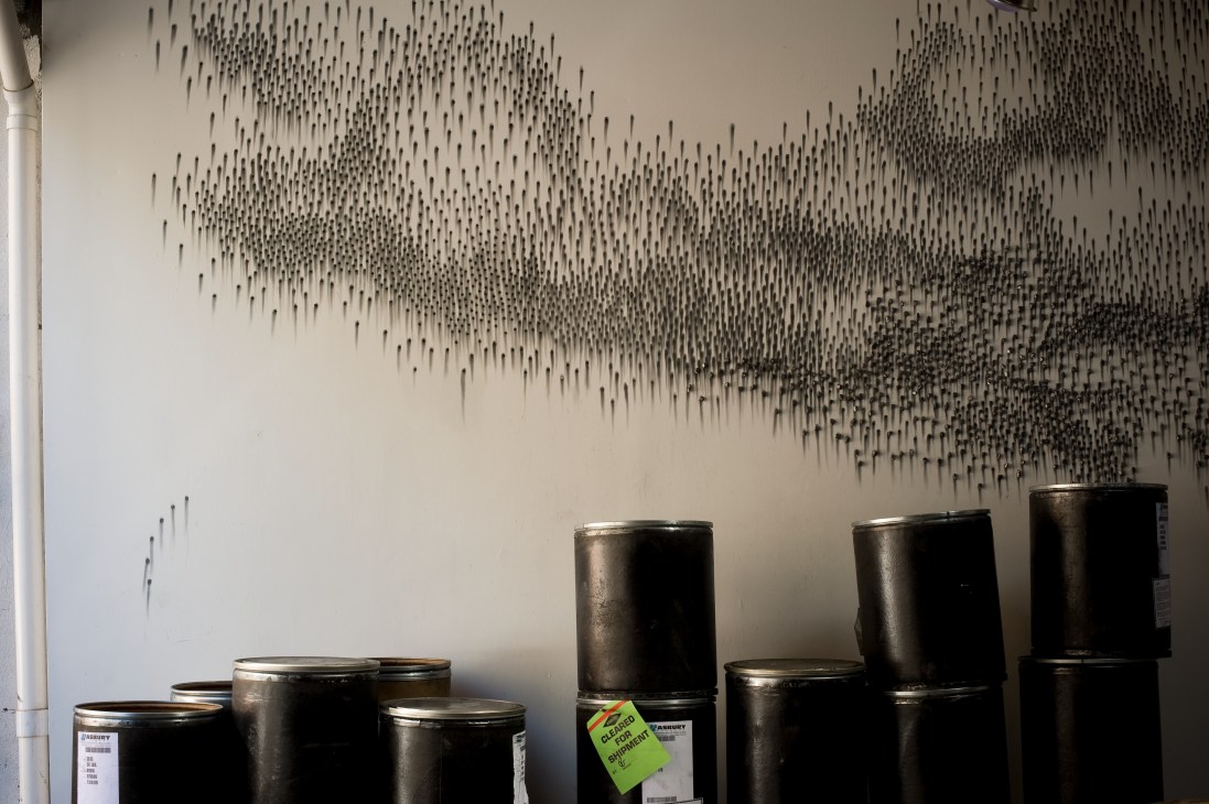 Wall installation of thousands of graphite sticks arranged in a pattern above empty black tubs labeled 'Elephant Expert'.