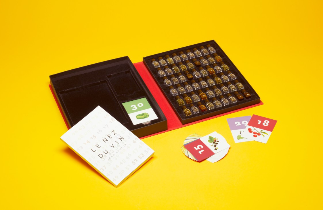 Le Nez du Vin wine tasting kit with multiple bottles in a box, booklet, and flash cards on yellow background.