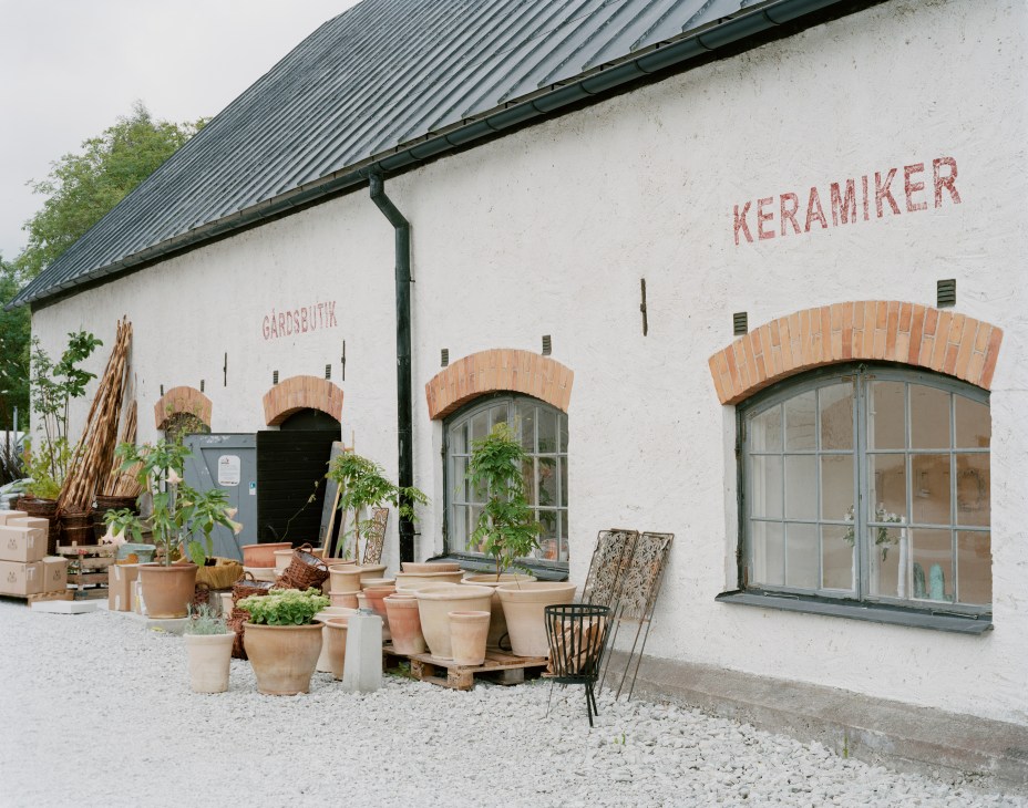 White-walled building with red brick arches displaying pottery and plants outside, labeled Keramiker.