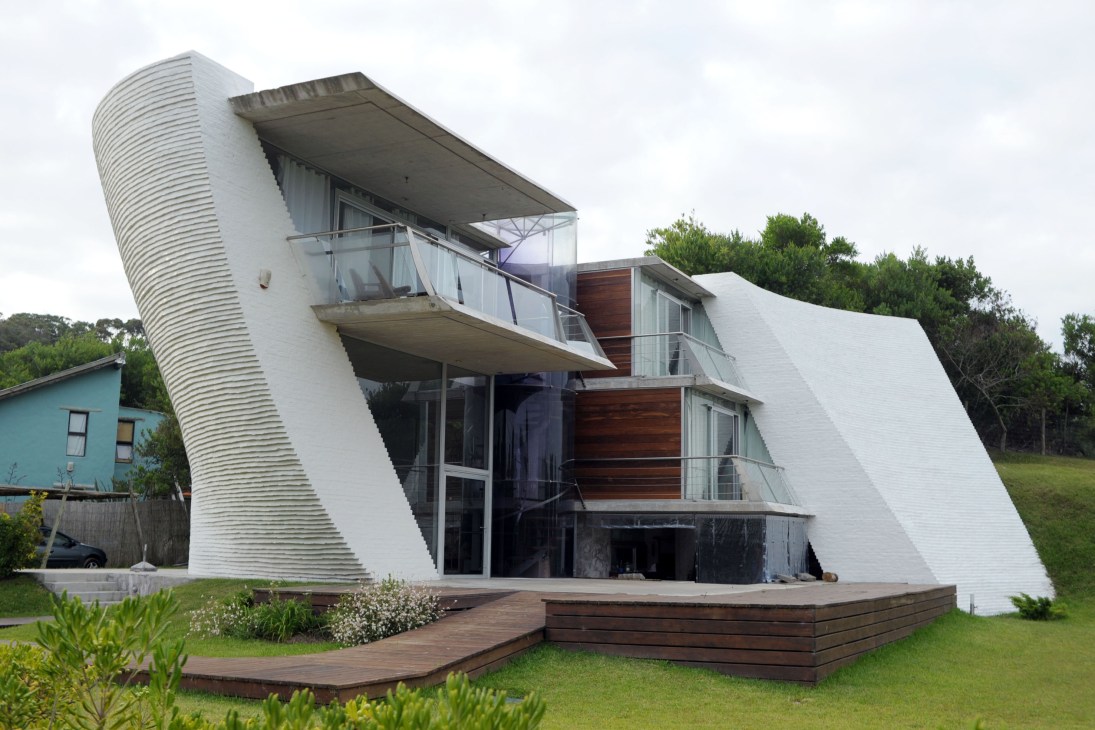 Modern white house with curved walls and wooden deck designed by architect Matías Sambarino in La Pedrera.