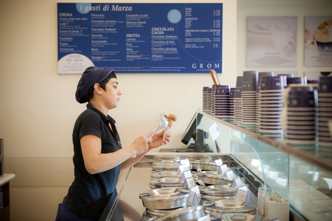 A Grom staff member prepares an ice cream cone at the counter.