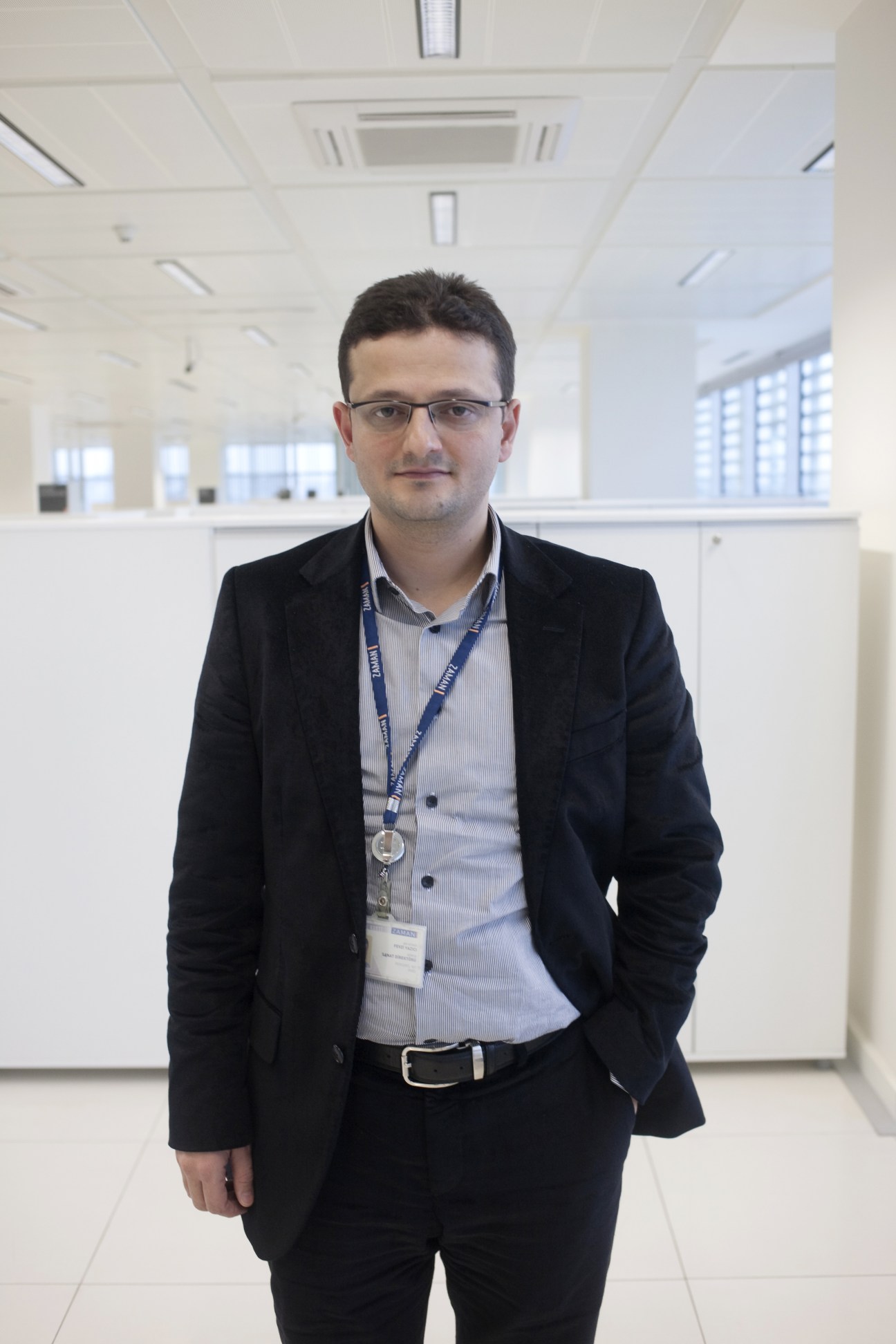 Fevzi Yazici, Zaman's art director, stands in a modern office wearing glasses, a dark blazer and ID badge.