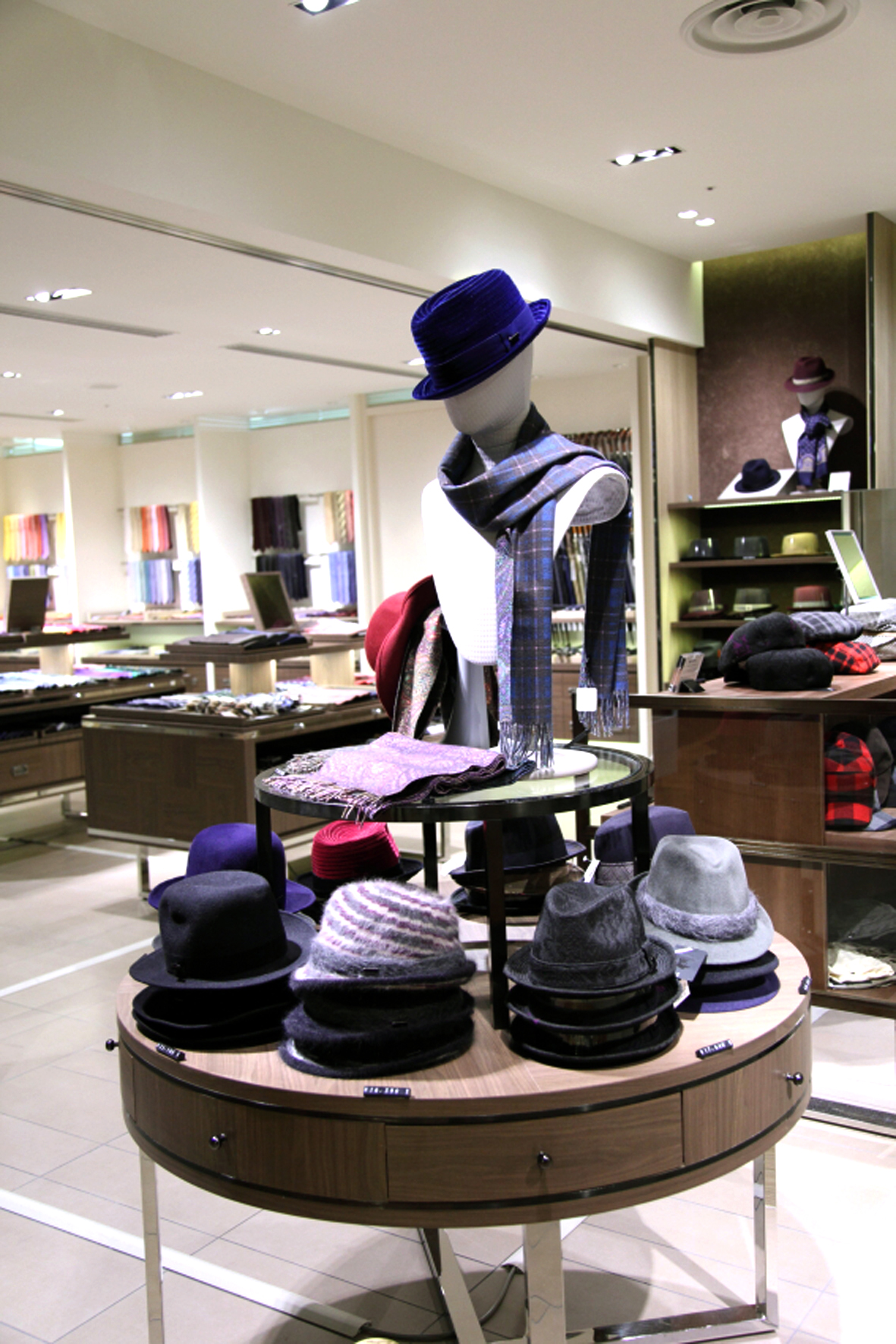 Mitsukoshi department store display with mannequin wearing blue hat and plaid scarf, surrounded by hats on circular table.